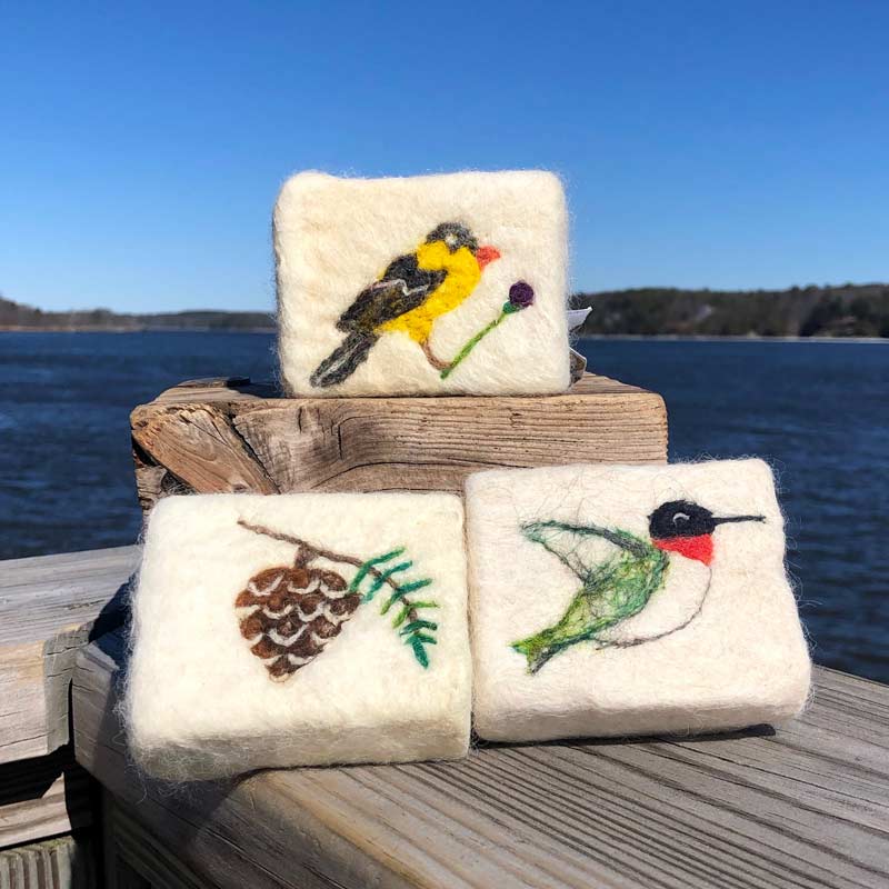 Alpaca Fleece, Felted Soaps with goldfinch, pinecone and hummingbird, sitting on a deck by the ocean.