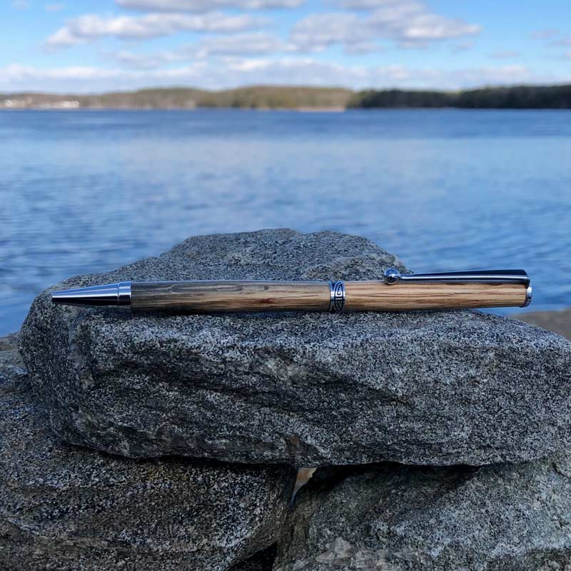 Lobster Trap Wood Pen, made from old, oak lobster traps, that have been retired by Maine lobstermen. It is laying on rocks by the ocean.